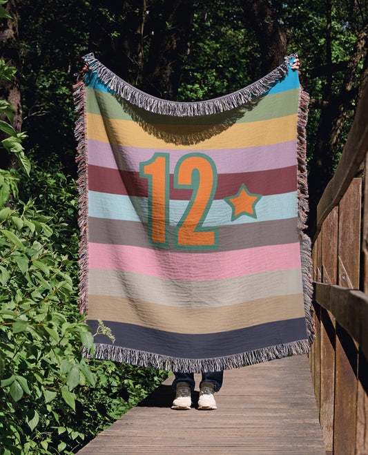 Colorful striped blanket with number 12 draped over a wooden railing in a forest setting