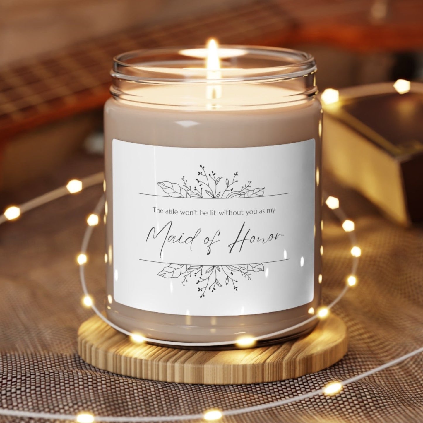 A picture of our 9 Oz Soy Candle with the label that says The Aisle wont be lit without you as my Maid of Honor. There are Beautiful floral border drawing on the top and bottom of the saying, in simple and elegant black ink color.