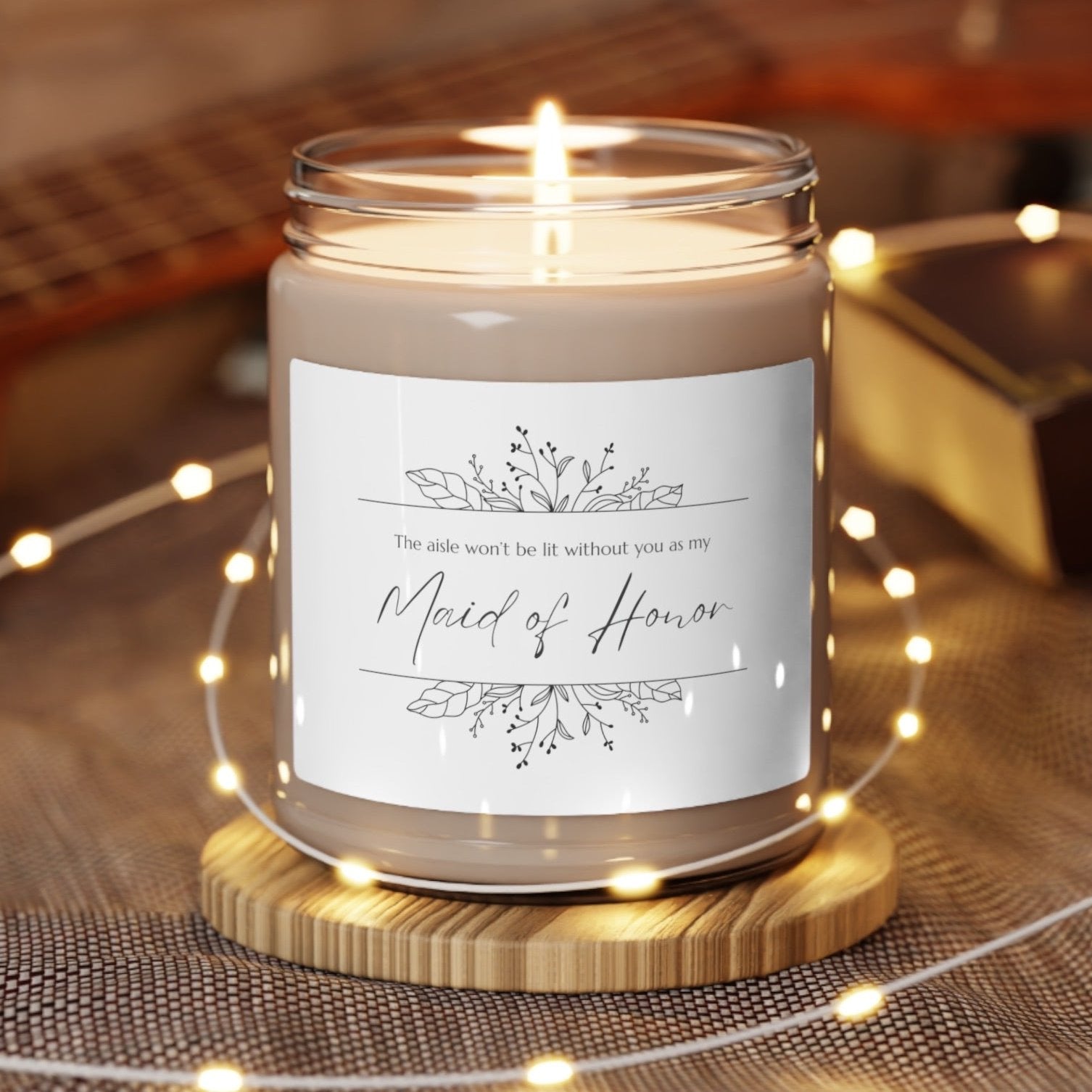 A picture of our 9 Oz Soy Candle with the label that says The Aisle wont be lit without you as my Maid of Honor. There are Beautiful floral border drawing on the top and bottom of the saying, in simple and elegant black ink color.