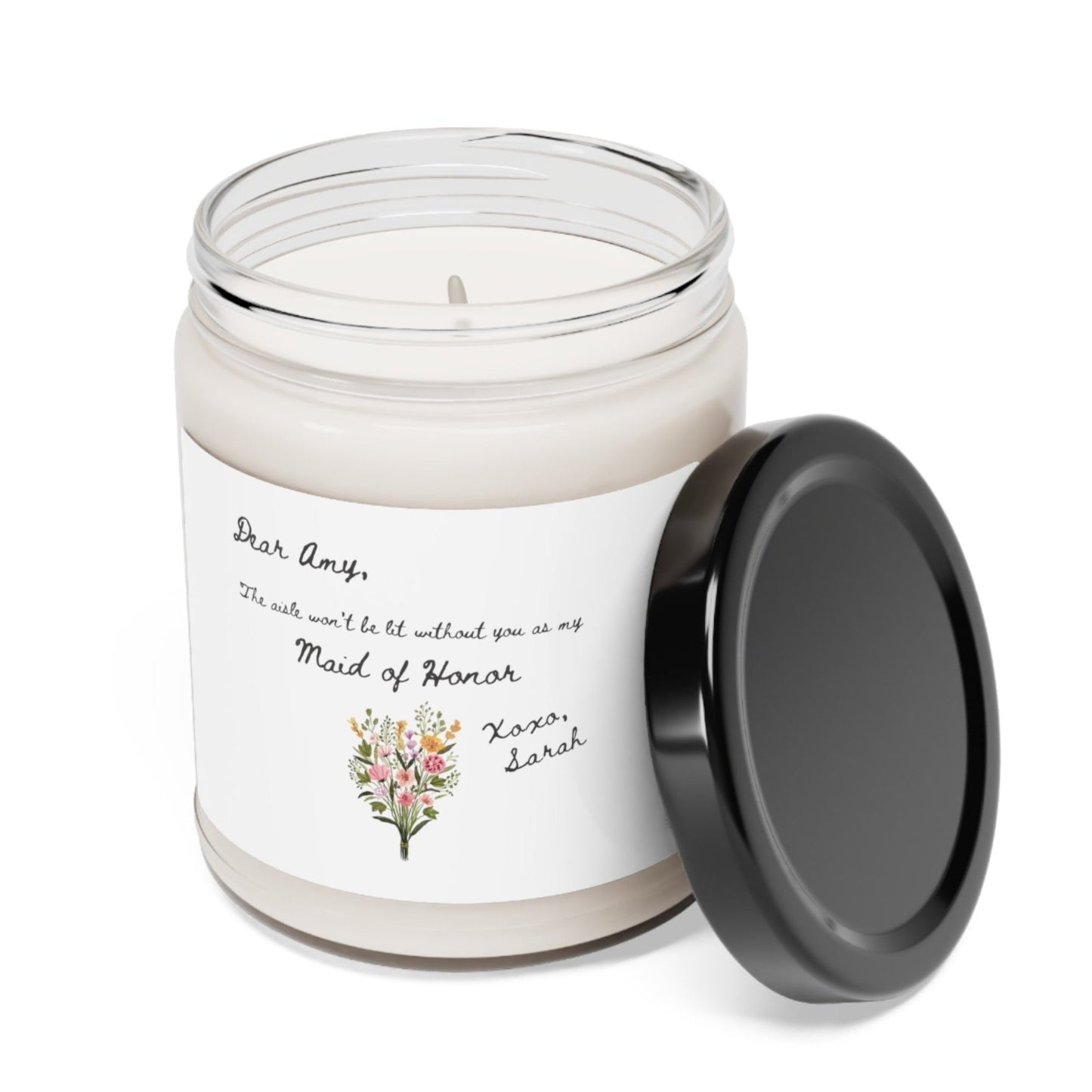 A picture of our 9 Oz Soy Candle with the label that says Dear Amy, The Aisle wont be lit without you as my Maid of Honor. Xoxo, Sarah. The names can be personalized. It is also adorned with an image of a beautiful bouquet of flowers.