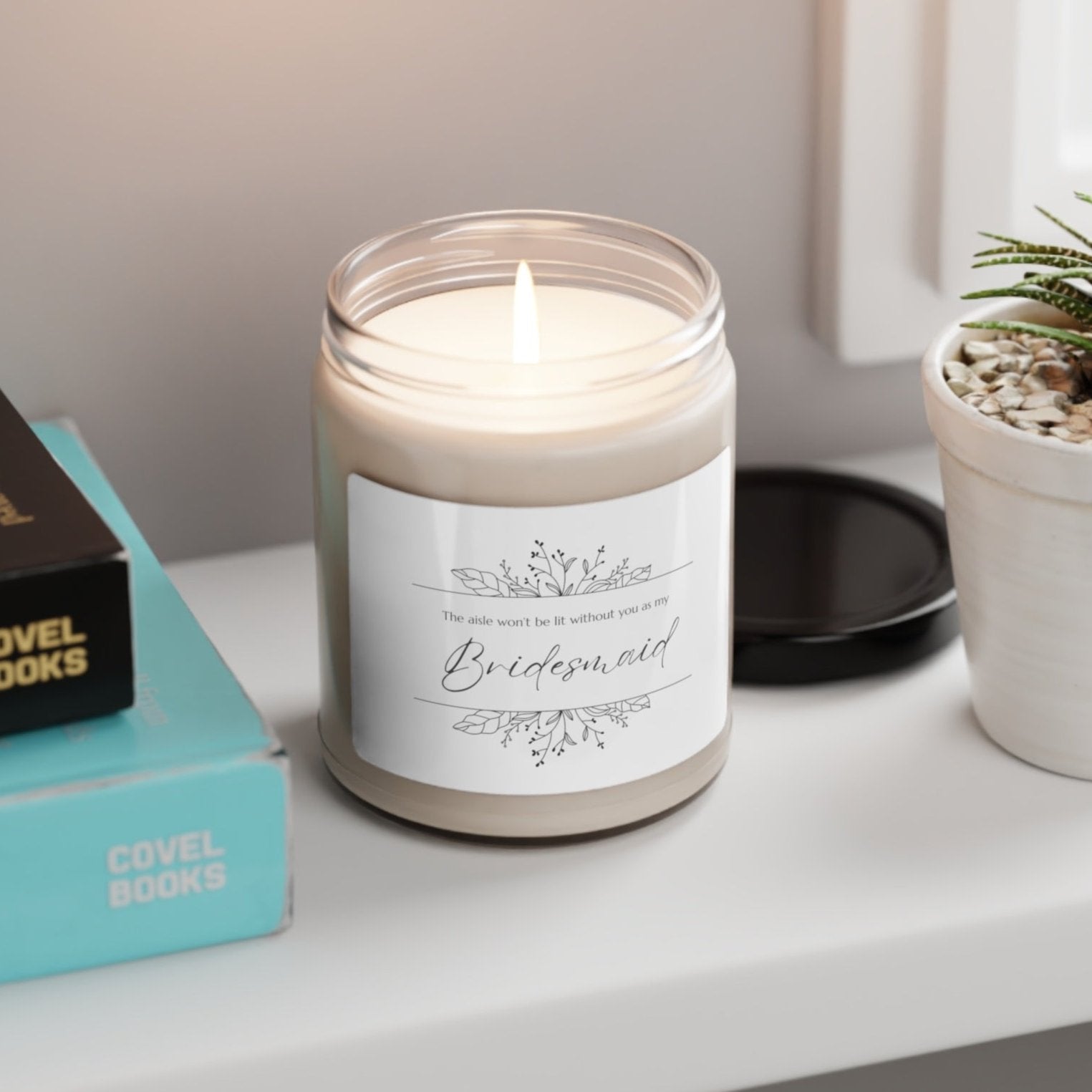 A picture of our 9 Oz Soy Candle with the label that says The Aisle wont be lit without you as my Bridesmaid. There are Beautiful floral border drawing on the top and bottom of the saying, in simple and elegant black ink color.