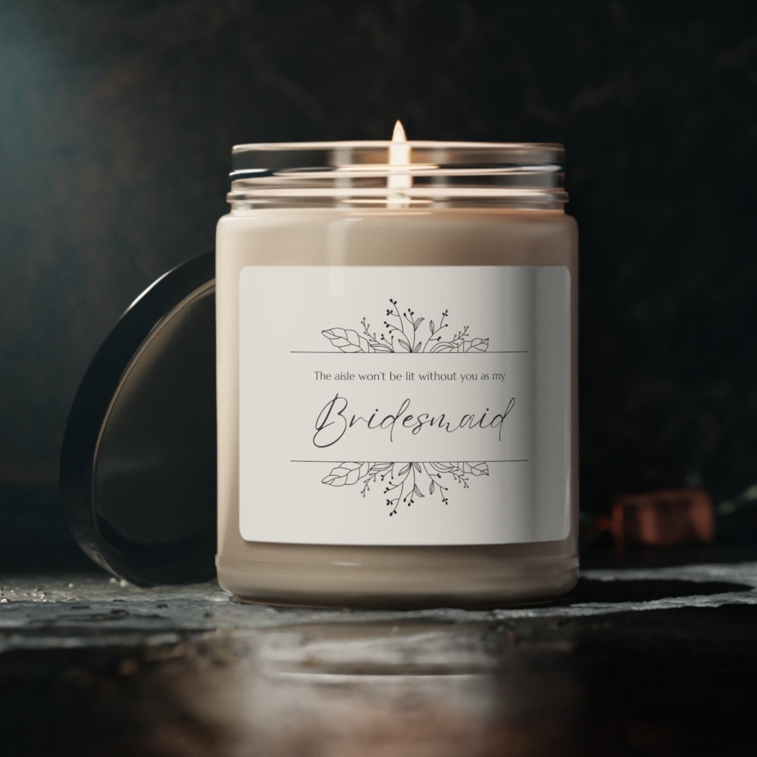 A picture of our 9 Oz Soy Candle with the label that says The Aisle wont be lit without you as my Bridesmaid. There are Beautiful floral border drawing on the top and bottom of the saying, in simple and elegant black ink color.