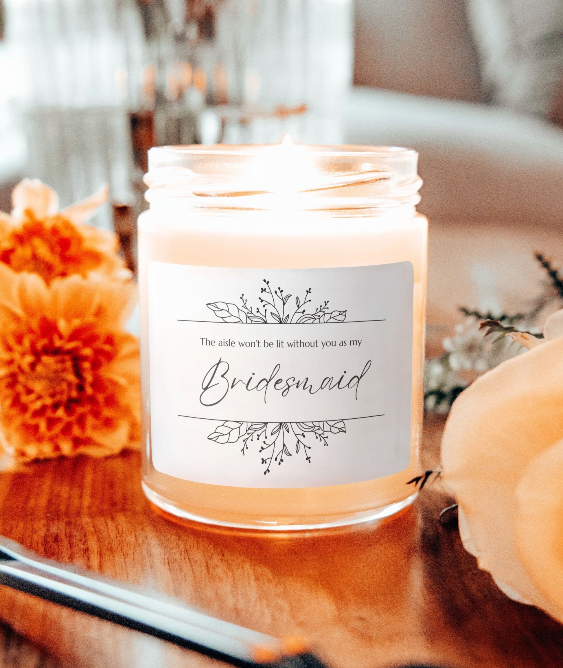 A picture of our 9 Oz Soy Candle with the label that says The Aisle wont be lit without you as my Bridesmaid. There are Beautiful floral border drawing on the top and bottom of the saying, in simple and elegant black ink color.