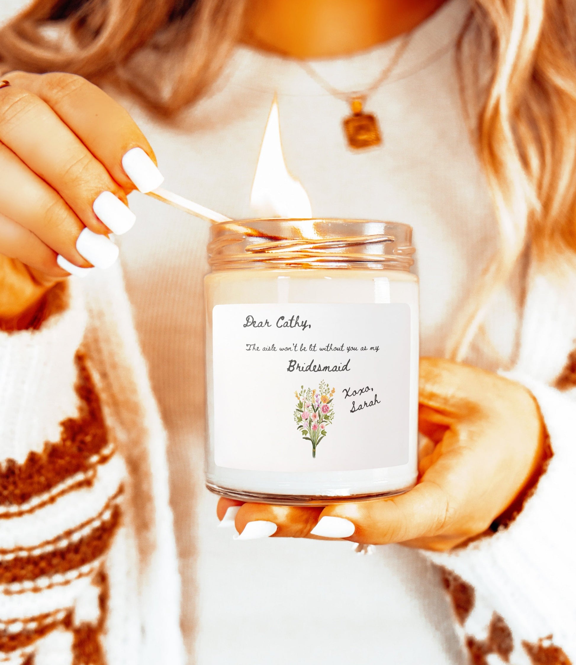 A picture of our 9 Oz Soy Candle with the label that says Dear Cathy, The Aisle wont be lit without you as my Bridesmaid. Xoxo, Sarah. The names can be personalized. It is also adorned with an image of a beautiful bouquet of flowers.