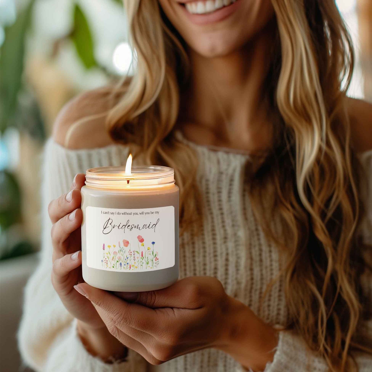 A picture of smiling woman holding our lit soy candle that says: I cant say I do without you, will you be my Bridesmaid. There is a lovely painted style wild flower graphic underneath the sayings.