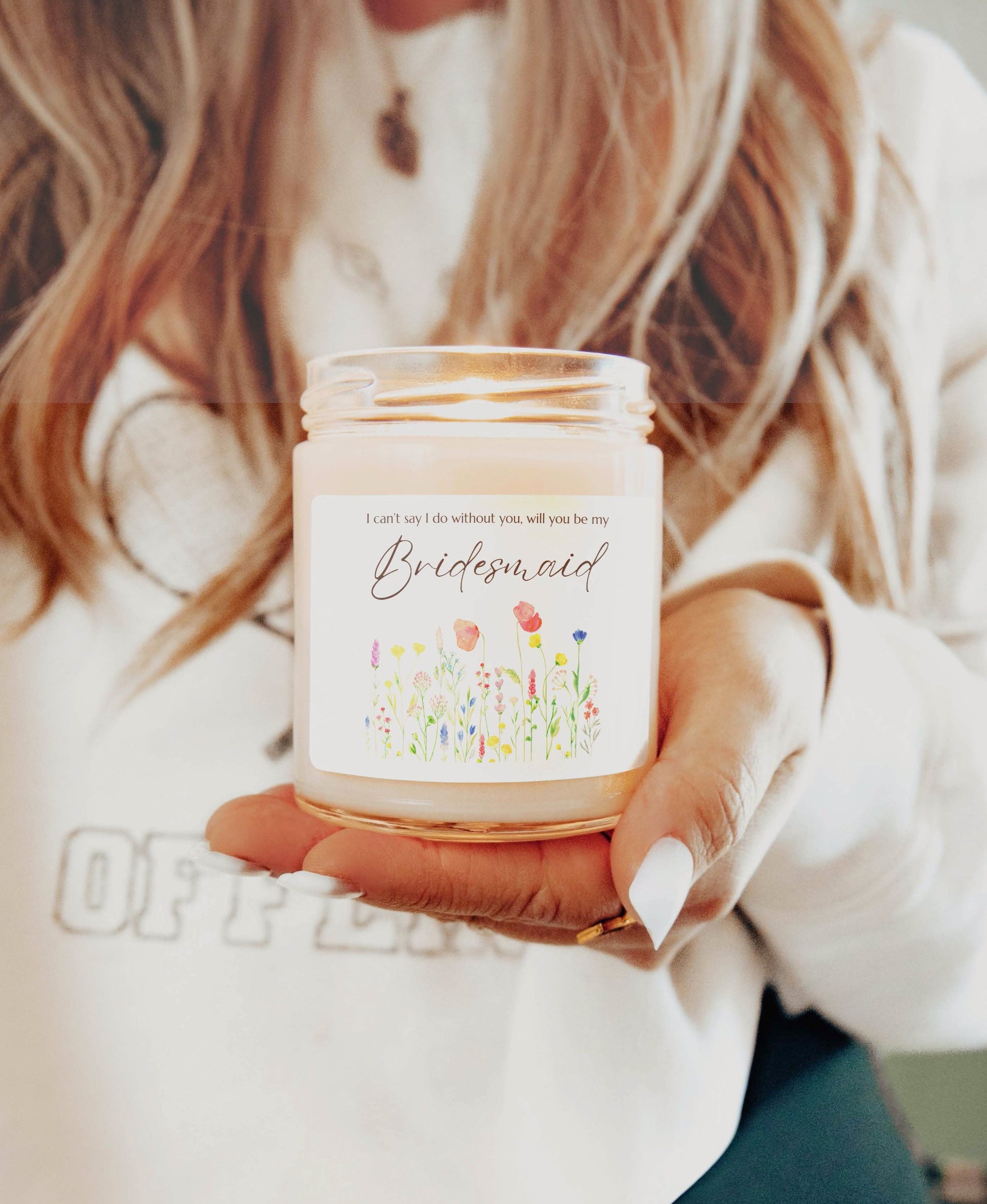 A picture of a glass jar of our lit soy candle that says: I cant say I do without you, will you be my Bridesmaid. There is a lovely painted style wild flower graphic underneath the sayings.