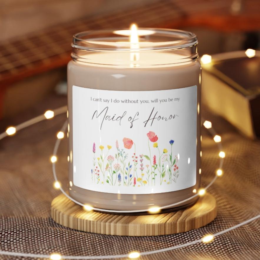 A picture of a glass jar of our lit soy candle that says: I cant say I do without you, will you be my Maid of Honor. There is a lovely painted style wild flower graphic underneath the sayings. The lid of the jar is black color.