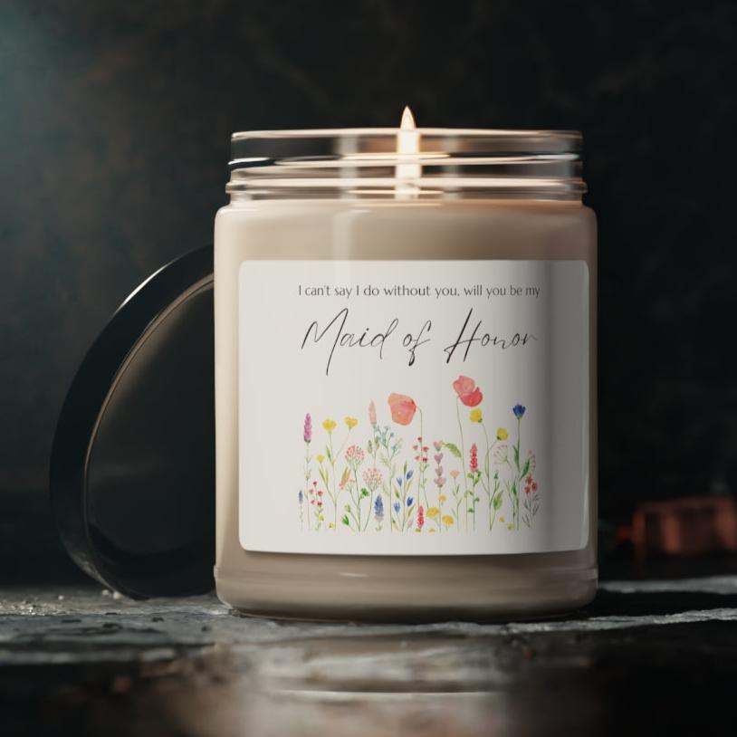 A picture of a glass jar of our lit soy candle that says: I cant say I do without you, will you be my Maid of Honor. There is a lovely painted style wild flower graphic underneath the sayings. The lid of the jar is black color.